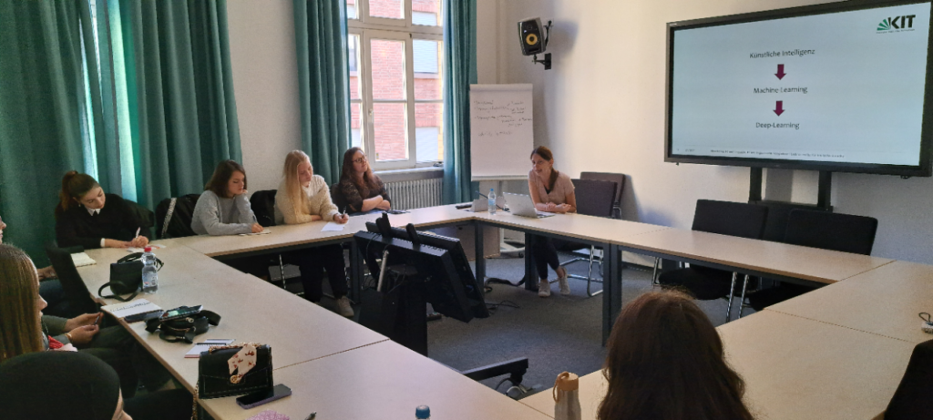 The image shows Nina Kalwa in a conference room. She is sitting at a conference Table together with several students whith whom she discusses.