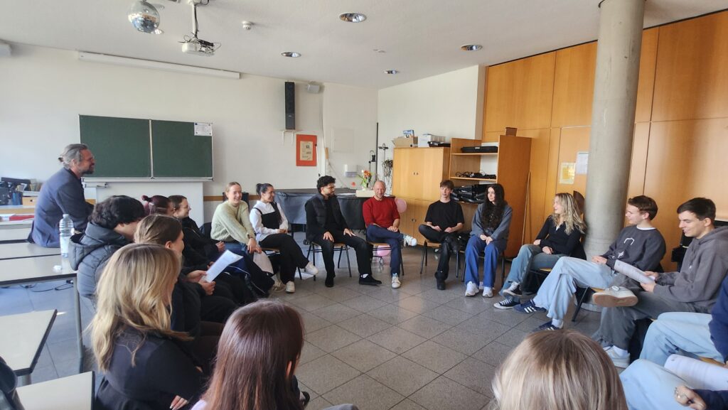 Personen sitzen in einem Klassenraum im Kreis und unterhalten sich angeregt.